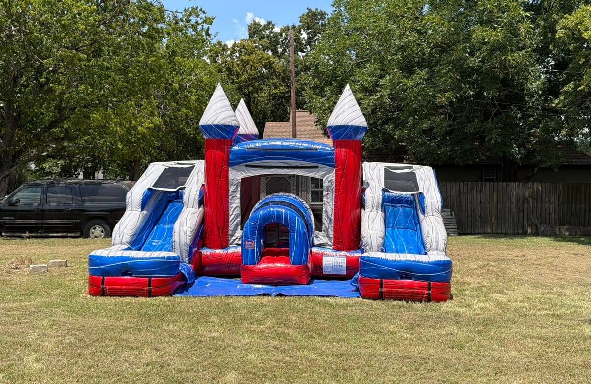 Red, white and blue inflatable castle with a slide on each side, set up in a yard