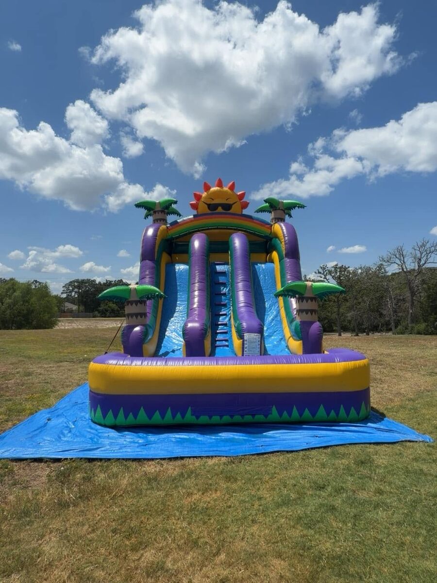 Purple water slide set up in an open field under a big blue sky